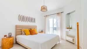 A bedroom with a bed, a bedside table, a hanging light fixture, a radiator, and a window with curtains. - Happy House in Clube Albufeira (Albufeira)