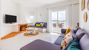 A modern living room with a sofa, a flat-screen TV, a fireplace, and a balcony with a view. - Happy House in Clube Albufeira (Albufeira)