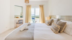A hotel room with a bed, a desk, a chair, a mirror, and a view of the outdoors. - Clube Albufeira, Family Holidays with Pool View (Albufeira)
