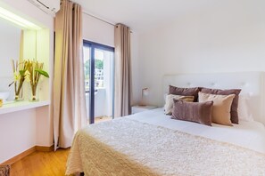 Quarto de hotel com uma cama grande, mesa de cabeceira, abajur, janela com cortinas e vista para o exterior.