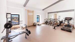 Ett gym med träningsutrustning, utsikt över en stad och en stor spegel.