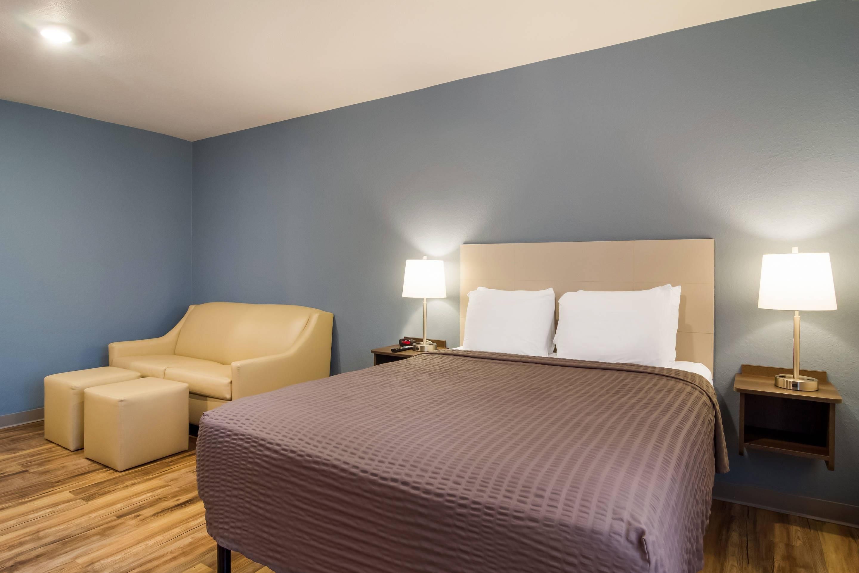 Una habitación de hotel con una cama, una silla, una mesita de noche y una lámpara.