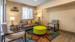 Un salon moderne comprenant un canapé, deux fauteuils, un pouf rond, un tapis à motifs et deux lampadaires.