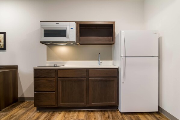 A kitchen with a built-in microwave, a sink, and a refrigerator. - WoodSpring Suites Jacksonville - South (Jacksonville)