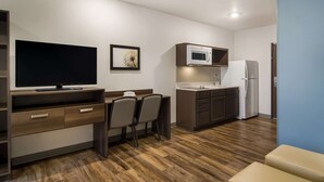 Cocina compacta con microondas, refrigerador y televisor de pantalla plana sobre un mueble de madera.