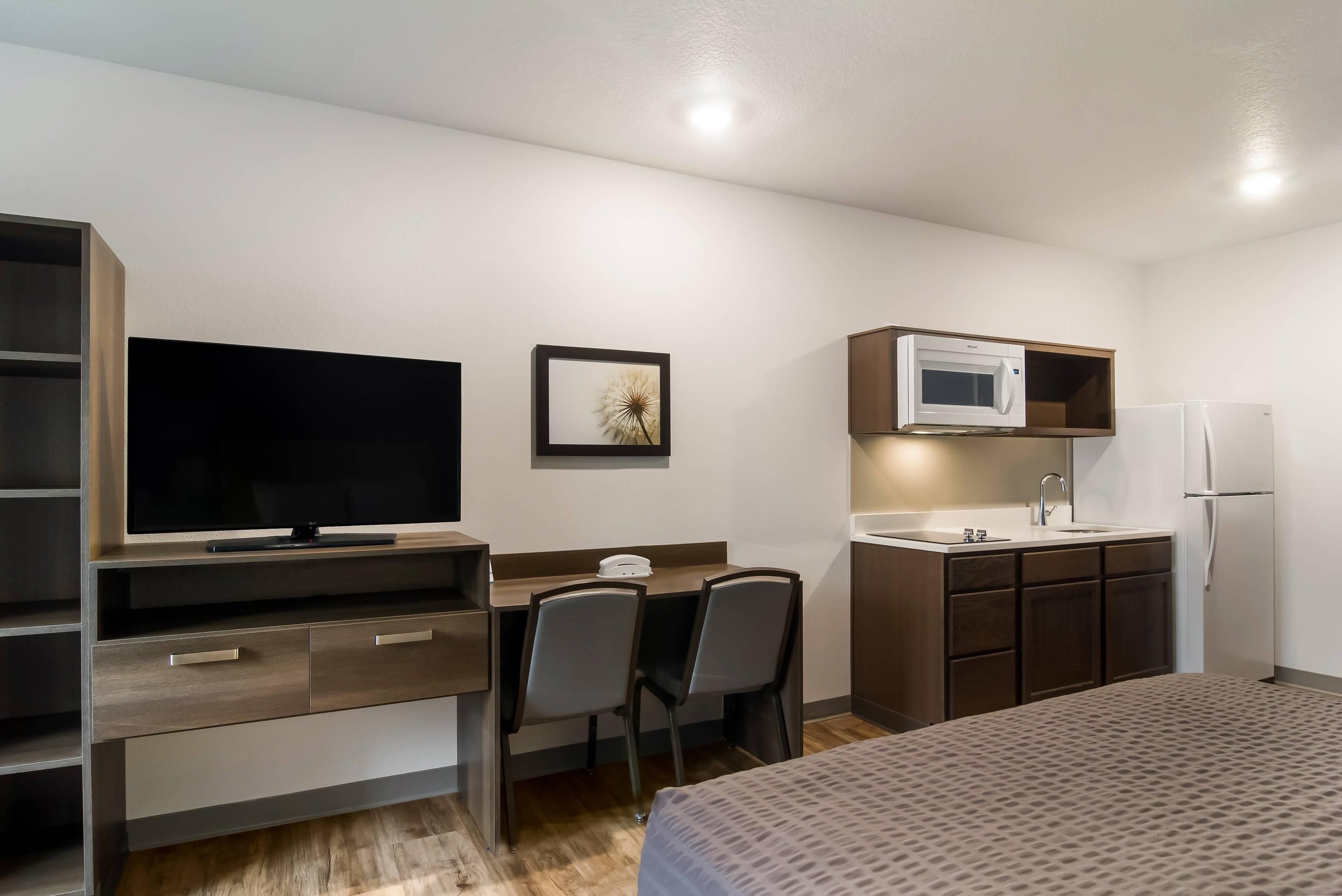 Habitación de hotel con cama, escritorio con silla, televisión, microondas, refrigerador y un lavamanos pequeño.