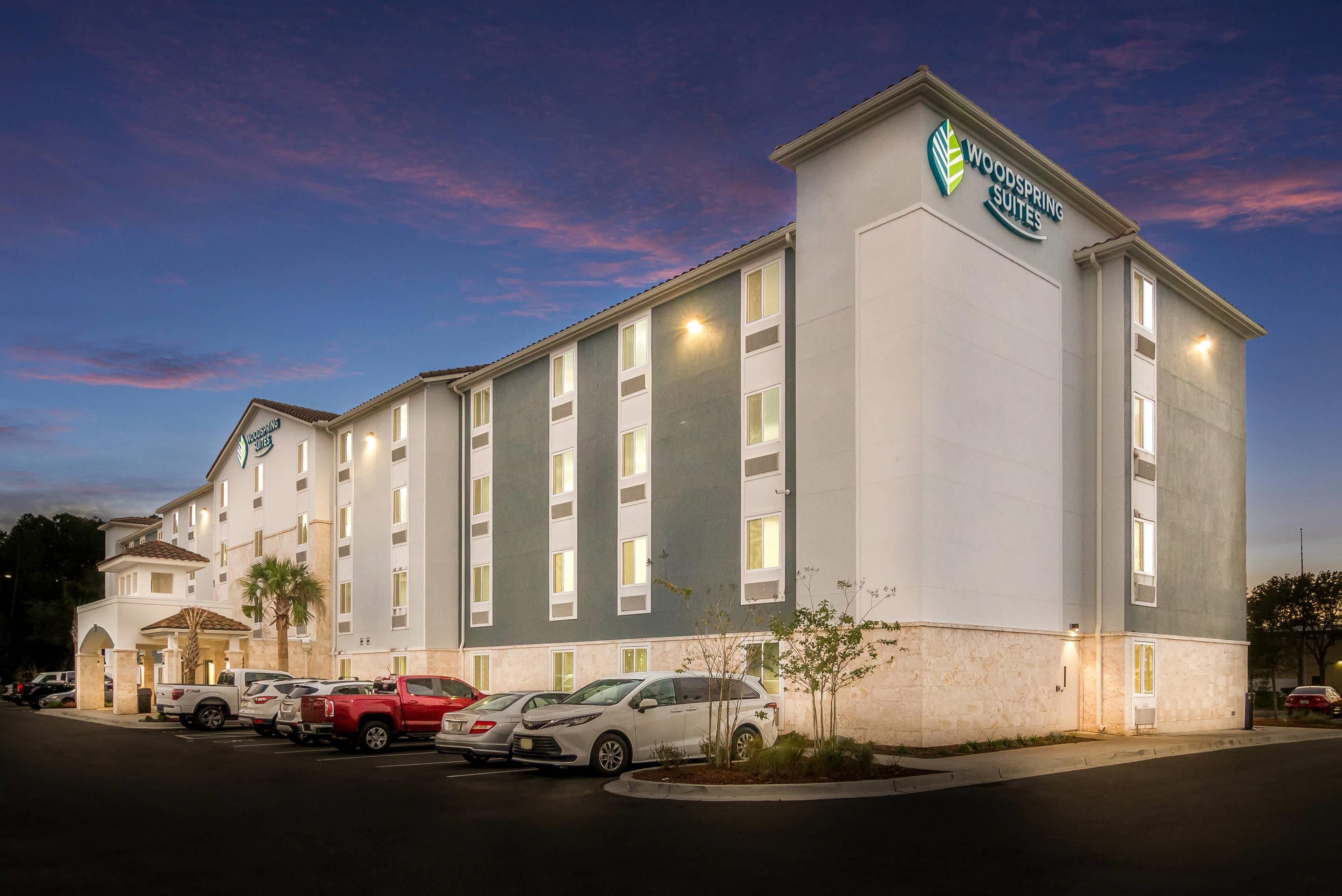 A multi-story hotel with a flat facade, a parking lot with several cars, and a clear sky.