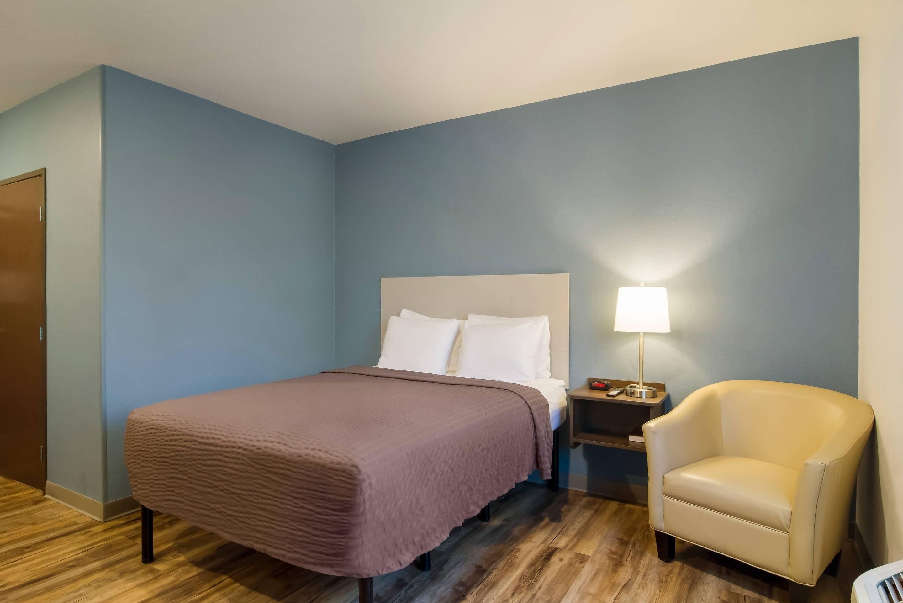 A hotel room with a bed, a nightstand, a lamp, and a chair.
