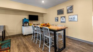 Un espace repas comprenant une table en bois et quatre chaises, un coin café et des œuvres d’art accrochées au mur.