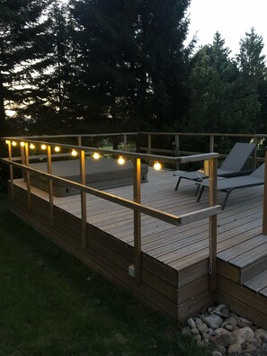 En træterrasse med gelænder, udendørs møbler og lyskæder.