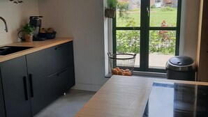 Eine moderne Küche mit Holzarbeitsplatte, schwarzen Schränken und einem großen Fenster mit Blick auf einen Garten und Häuser.