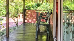 Un espacio al aire libre techado con paja, una mesa con sillas y vista a la vegetación.