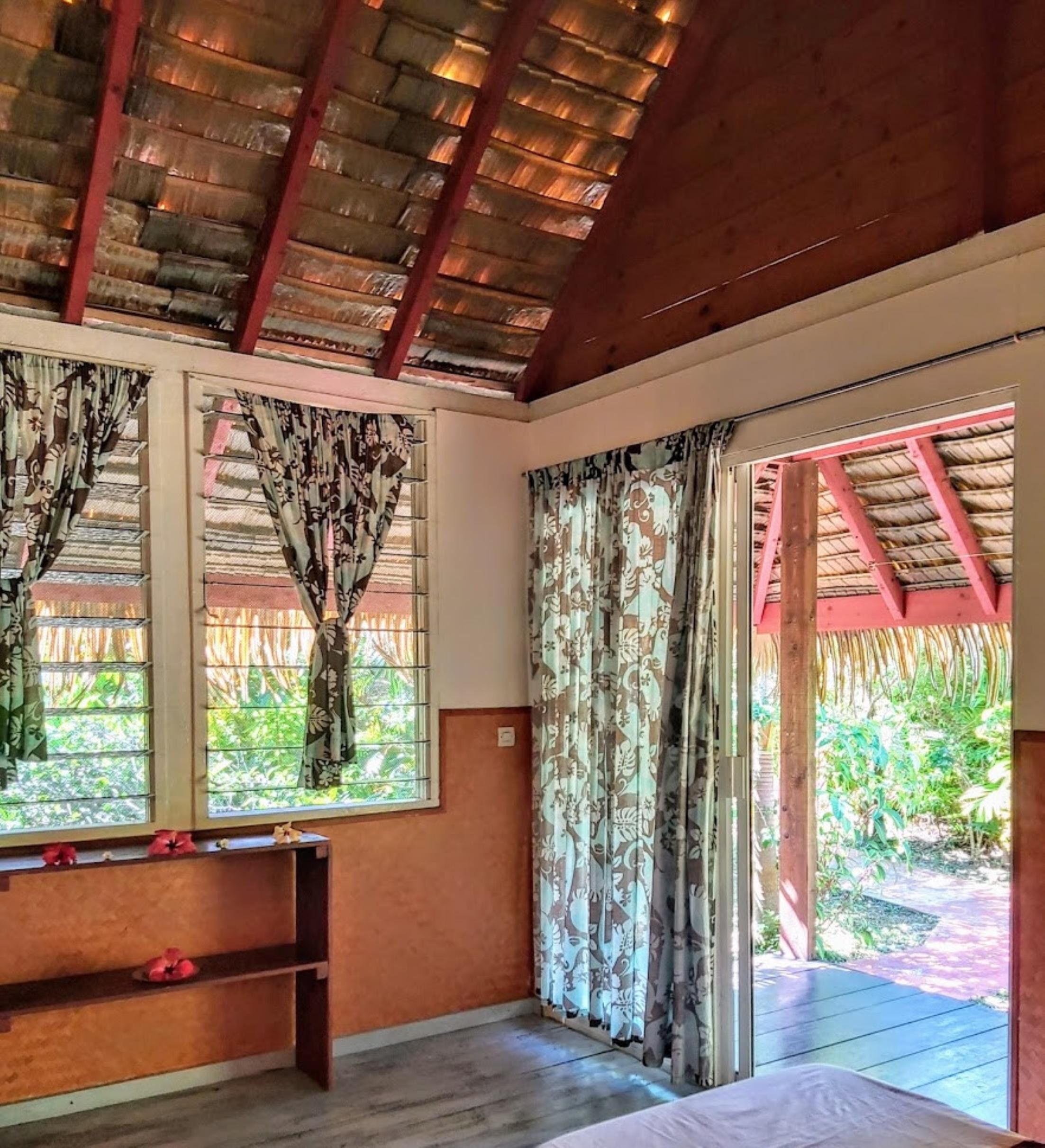 Une pièce avec un plafond en bois, un lit, un banc et une fenêtre avec des rideaux.