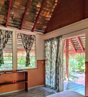 Ein Zimmer mit Holzboden, einem Bett, einer Bank und einem Fenster mit Vorhängen.