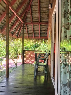 Un espace extérieur abrité, doté d’un toit de chaume, d’une table avec des chaises et offrant une vue sur la verdure.