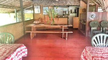 Un restaurant avec des tables et des bancs en bois, un toit de chaume et des chaises en plastique.