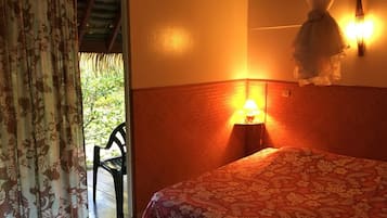 Ein Zimmer mit einem Bett, einem Nachttisch, einer Lampe, einem Sessel und Blick auf Grünflächen.