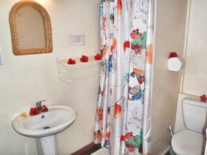 Un baño con lavamanos blanco, un espejo, inodoro y cortina de ducha con motivos florales.