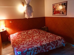 A bedroom with a bed covered in a floral-patterned bedspread, a bedside table with a lamp, and a wall-mounted light fixture.