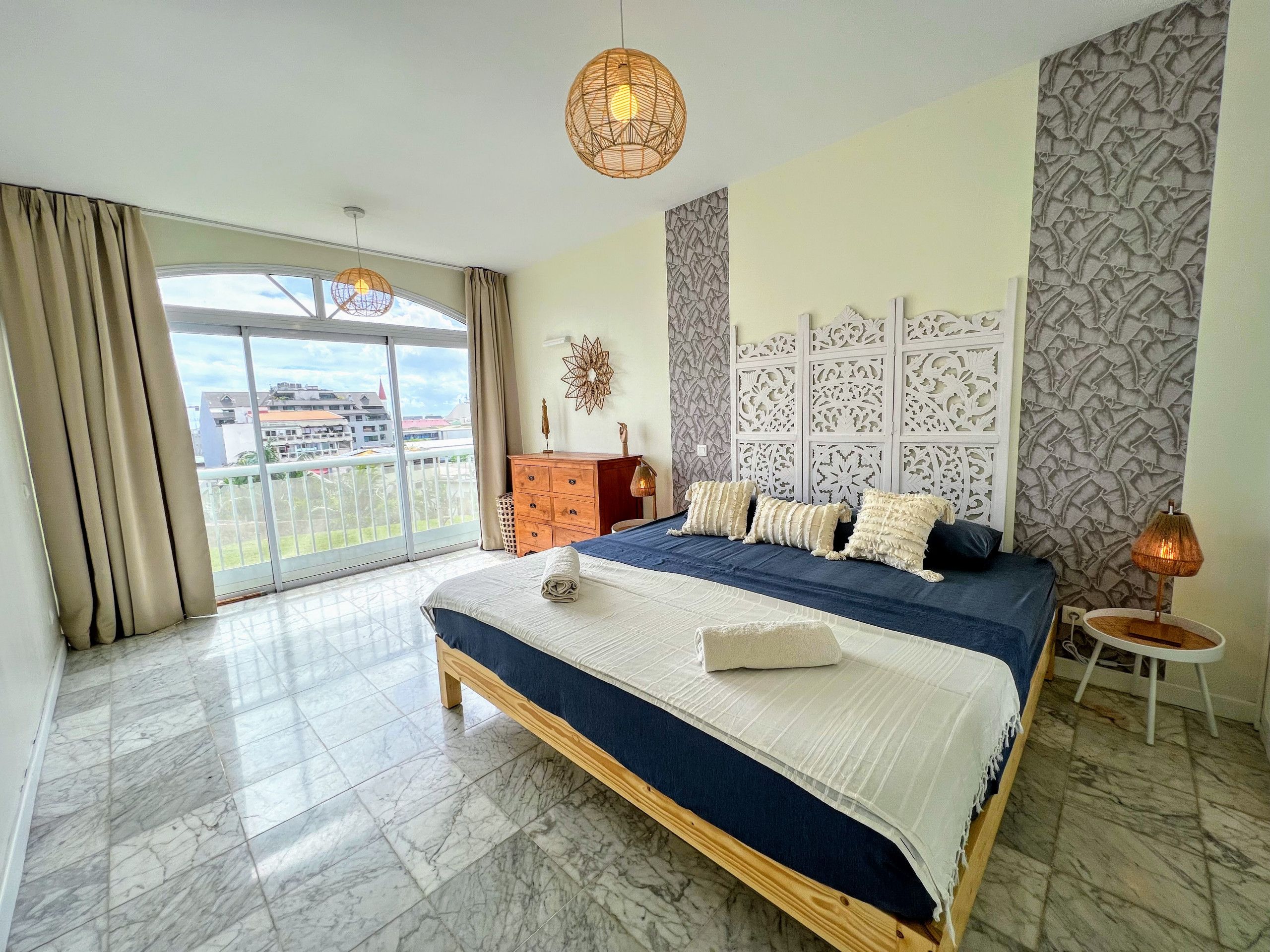 Un dormitorio amplio con una cama grande, vista a través de un ventanal corredera y un panel decorativo en la pared.