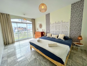 A spacious bedroom with a large bed, a view through a sliding glass door, and a decorative wall panel. - TAHITI - Orovini Cottage (Papeete)