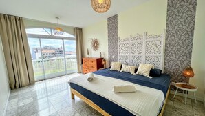 Une chambre spacieuse avec un grand lit, une vue dégagée grâce à une porte-fenêtre coulissante et un panneau décoratif mural.