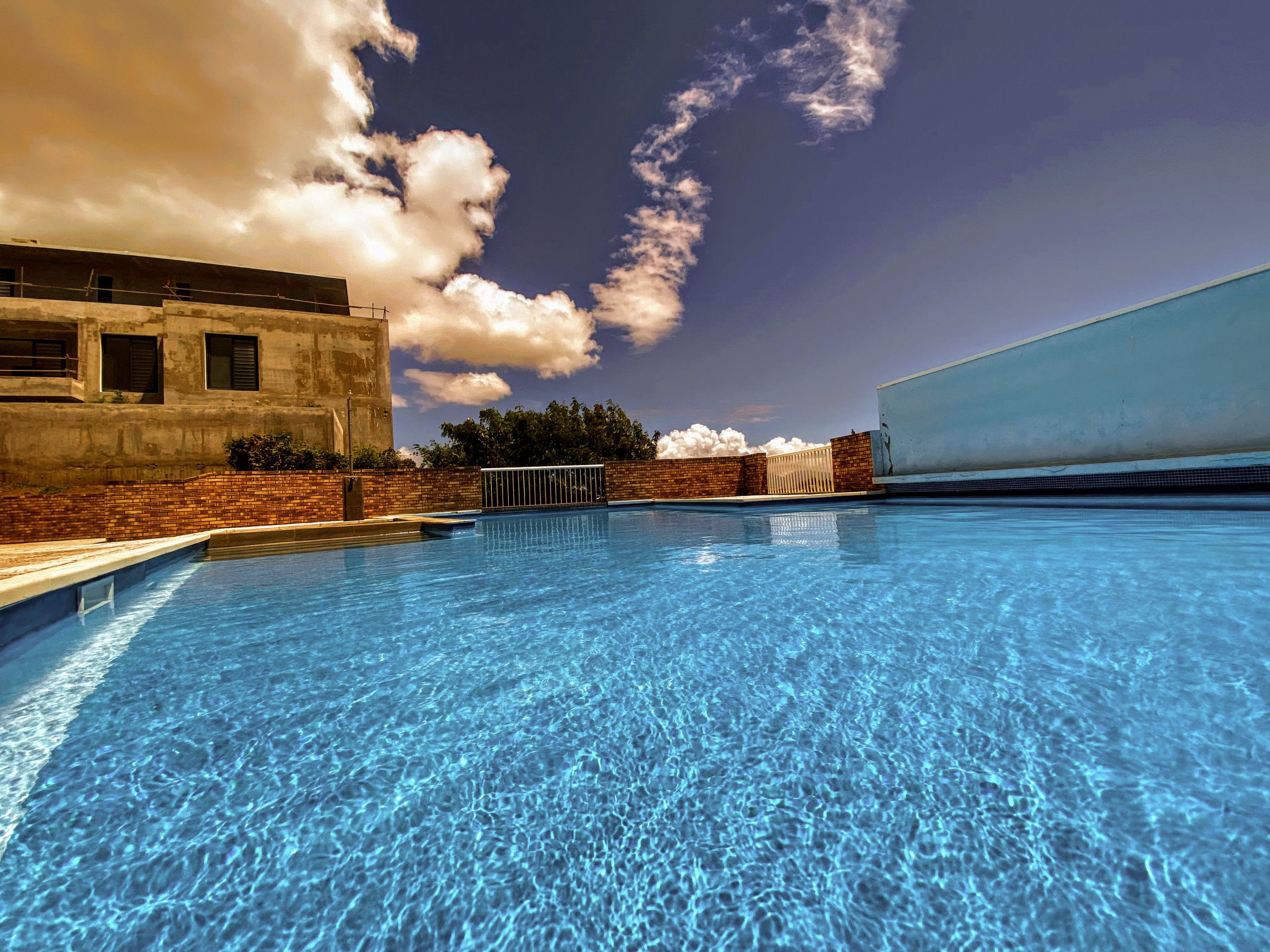 A swimming pool with clear blue water, surrounded by a brick wall and a white building.