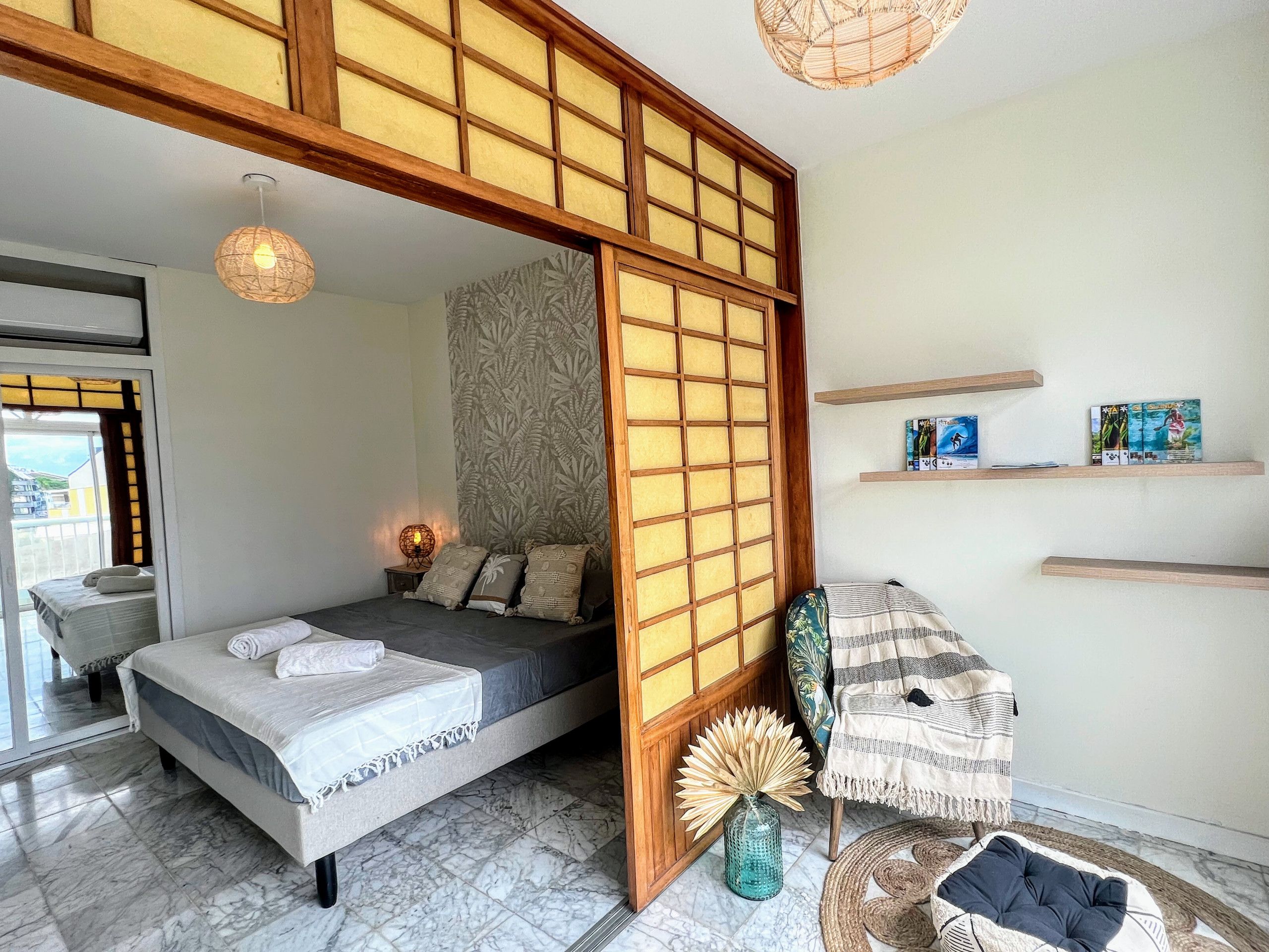 A room with a bed, a wooden partition, a shelf with books, and a decorative vase.