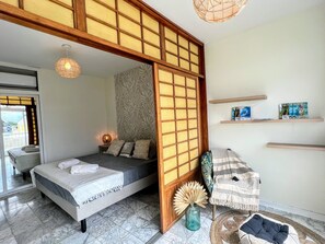 A room with a bed, a wooden partition, a shelf with books, and a decorative vase. - TAHITI - Orovini Cottage (Papeete)