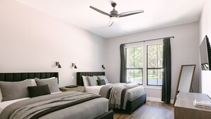 Ein modernes Schlafzimmer mit zwei Betten, einem Deckenventilator, einem großen Fenster mit Vorhängen und einem Schreibtisch mit Spiegel.