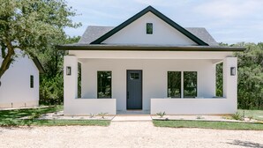 Ein modernes eingeschossiges Haus mit weißer Fassade, dunklem Dach und einer Veranda.