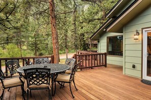 Eine Holzterrasse mit rundem Tisch und Stühlen, umgeben von Bäumen.