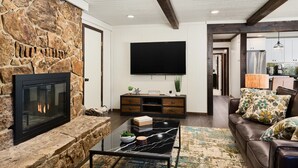Una sala de estar con chimenea de piedra, televisor de pantalla plana, sofá de cuero y una mesa de centro.