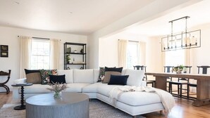 A spacious living room with a light-colored sectional sofa, a round coffee table, and a wooden dining table with chairs. - Luxurious Nantucket Getaway | Heated Pool (Nantucket)