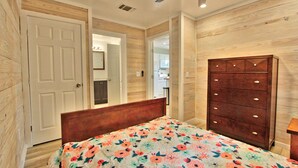 Un dormitorio con piso de madera, una cama con colcha floral, un tocador de madera y un ventilador de techo.