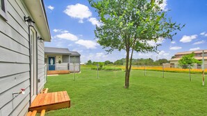 Un patio trasero con terraza de madera, un árbol y una casa con puerta azul.