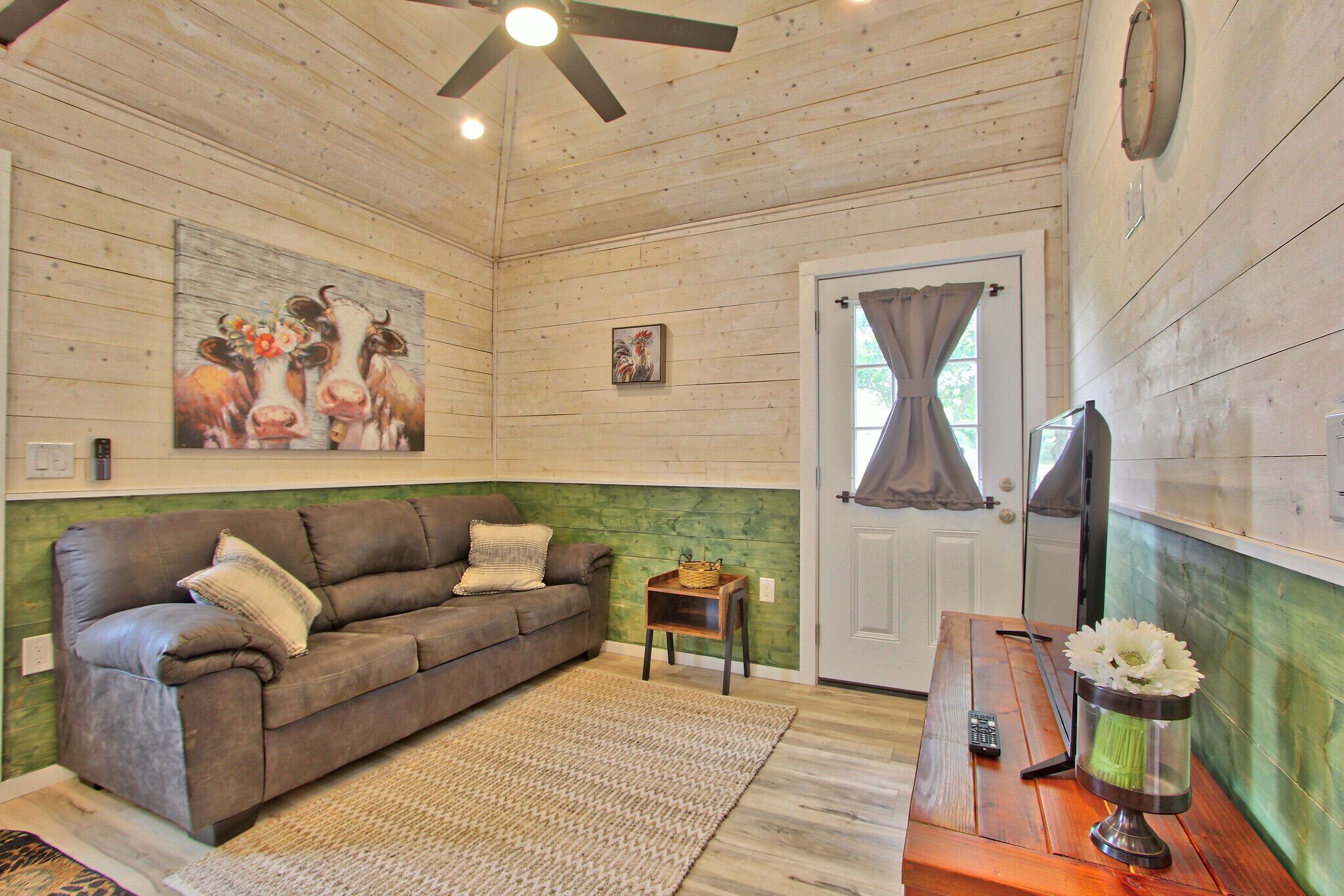 A cozy room with a wooden ceiling, a brown leather sofa, a small wooden table, and a door with curtains.