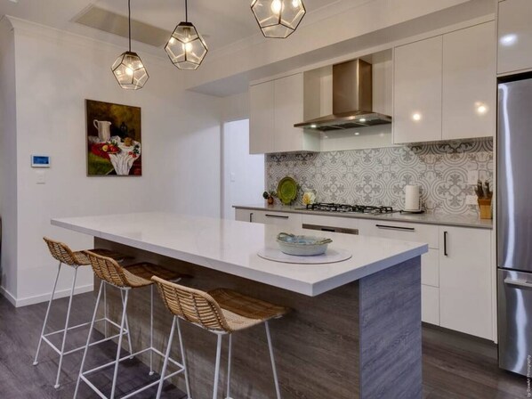A modern kitchen with a large island, white cabinets, a gas stove, and a stainless steel refrigerator.