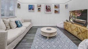 Una sala de estar moderna con un sofá, una mesa de centro redonda, un televisor sobre un mueble de madera y obras de arte enmarcadas en la pared.