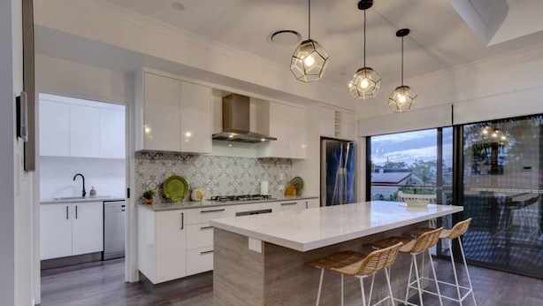 Una cocina moderna con una isla grande, armarios blancos y vistas a través de un ventanal.