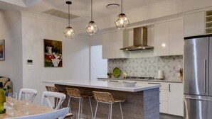 Una cocina moderna con una isla central, taburetes de bar, un refrigerador de acero inoxidable e iluminación colgante.