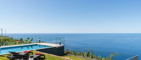 A swimming pool with lounge chairs and a view of the ocean.