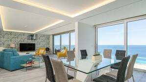 Ein modernes Wohnzimmer mit einem Glastisch, bequemen Sitzmöglichkeiten, einem Flachbildfernseher und einem großen Fenster mit Meerblick.