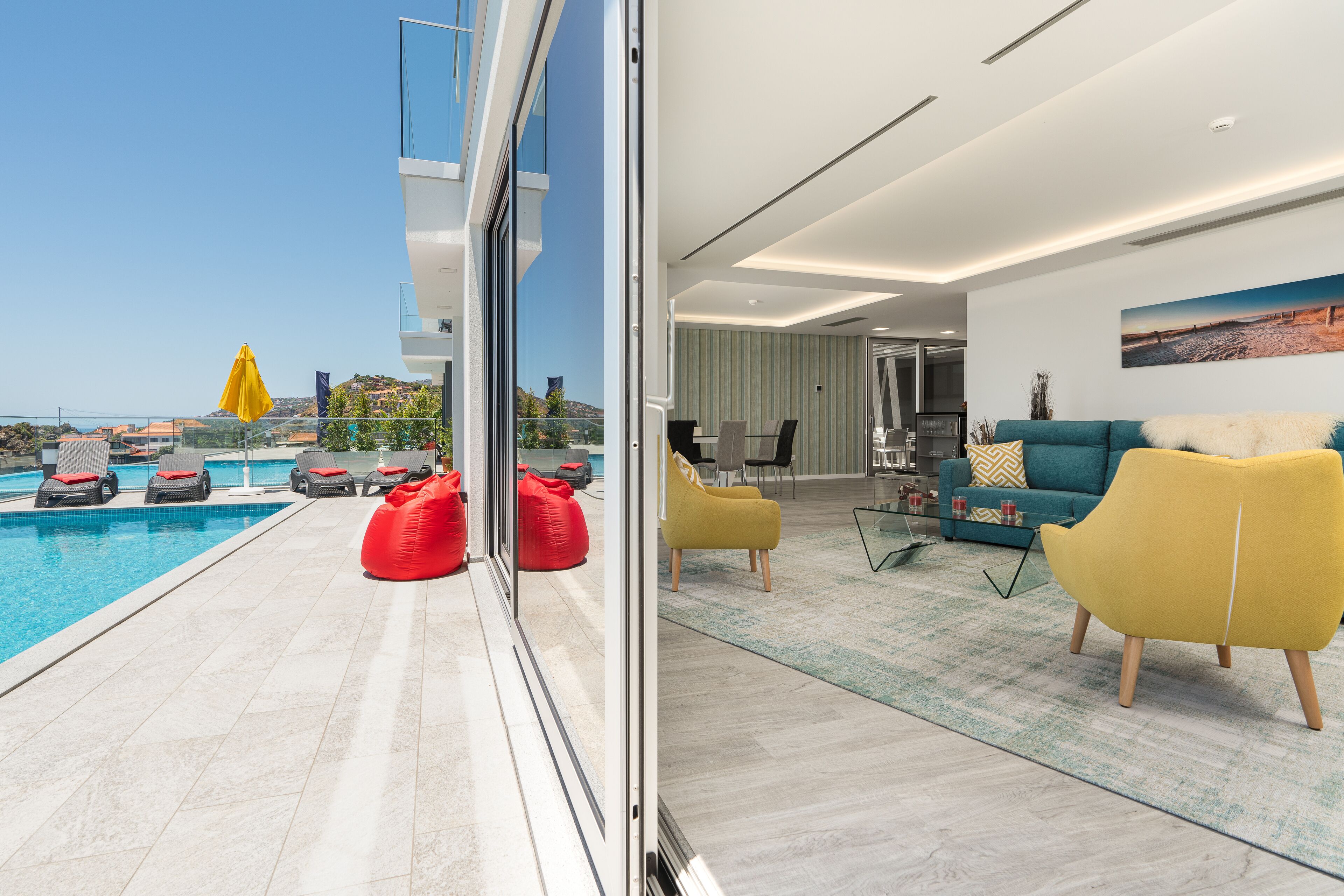 Un espace de vie moderne avec une piscine, des fauteuils en forme de haricot rouge et un canapé turquoise.