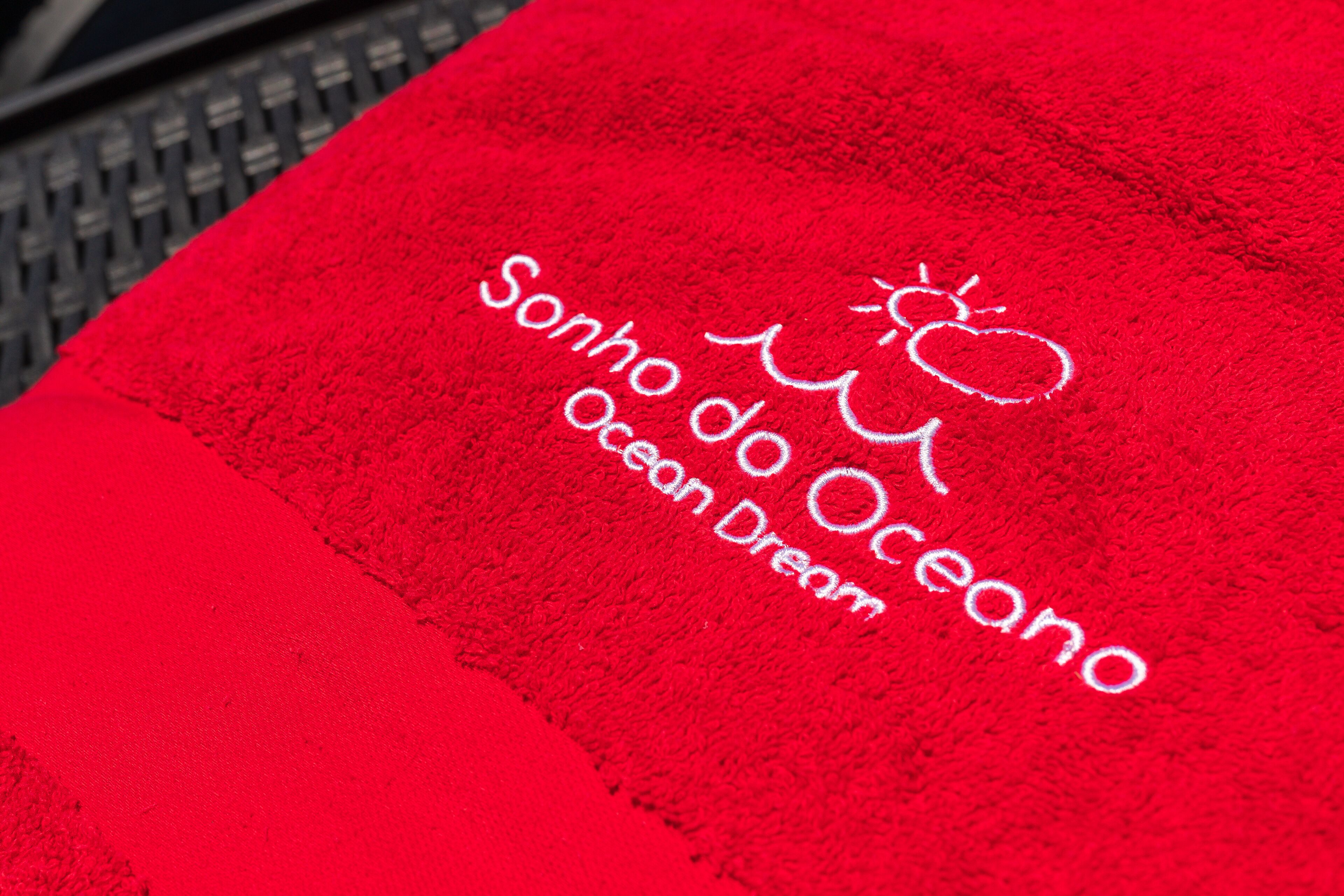 Et rødt håndklæde med teksten "Sonho do Oceano Ocean Dream" og et sol- og bølgesymbol.