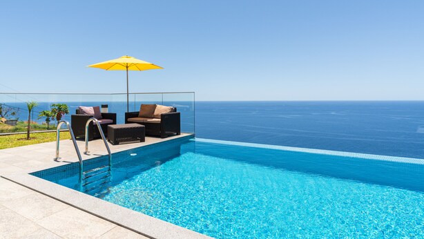 Ein Pool ohne Ende mit freiem Blick auf den Ozean, ein gelber Sonnenschirm und Sitzgelegenheiten im Freien.