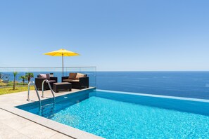 An infinity pool with a clear view of the ocean, a yellow umbrella, and outdoor seating. - Sonho do Oceano (Ribeira Brava)