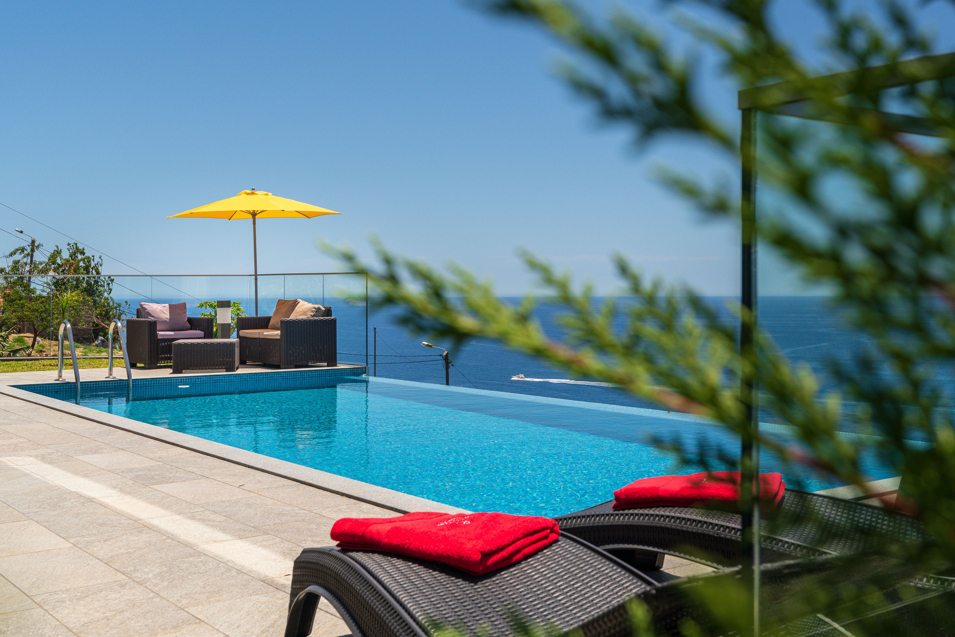 A poolside area with lounge chairs and a yellow umbrella, overlooking the sea.