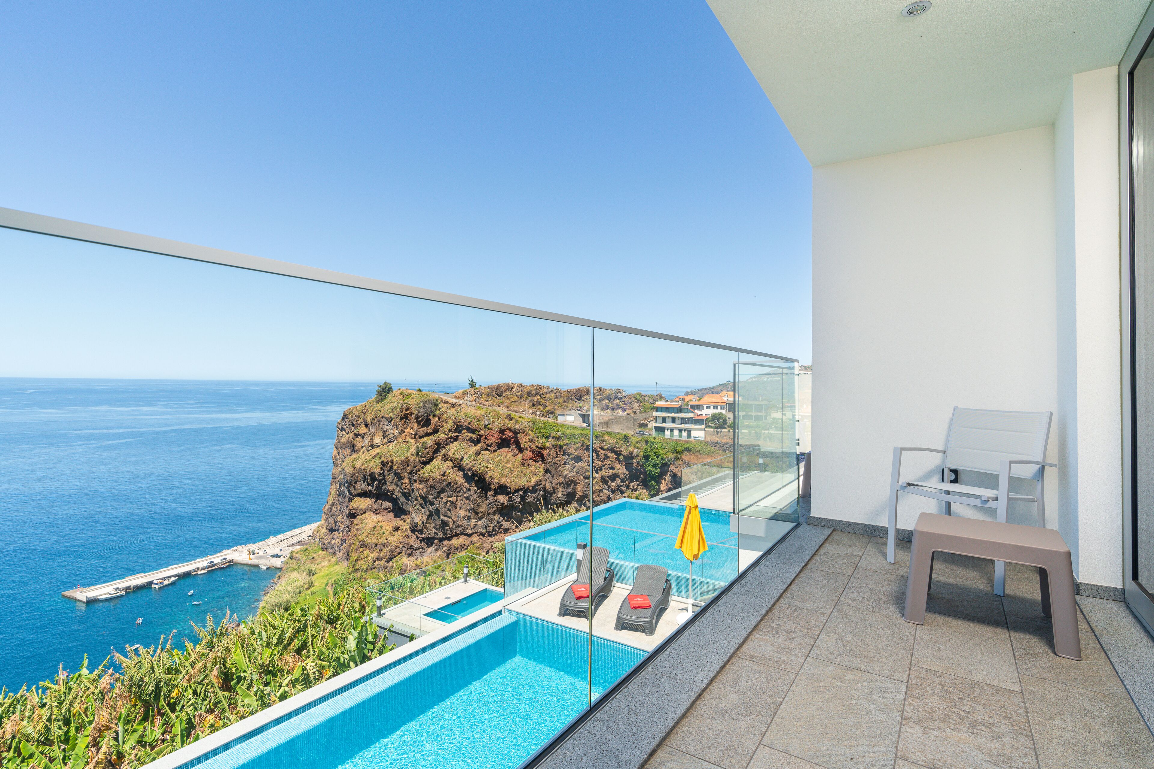 A balcony with a glass railing overlooking a pool and the ocean.