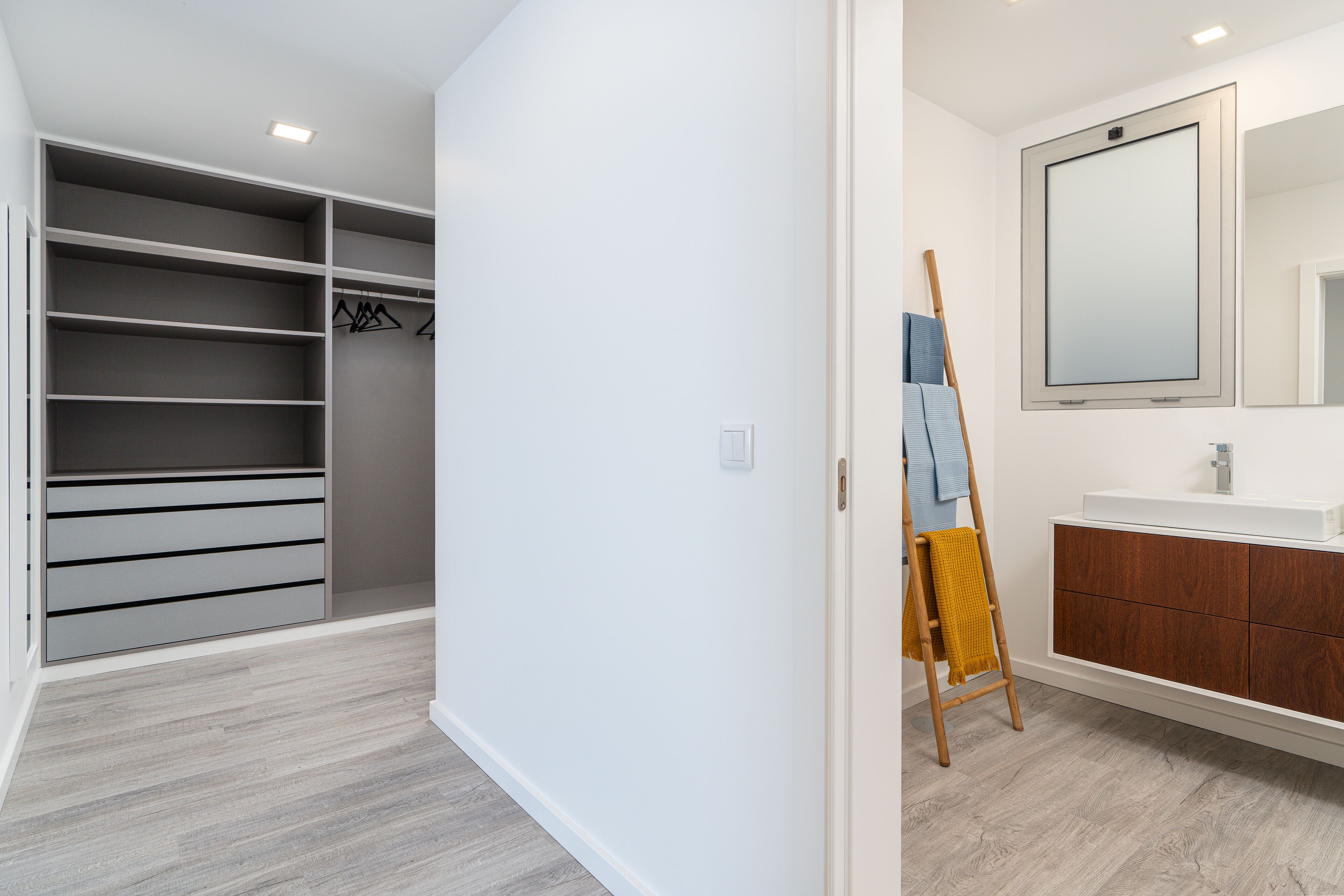 A modern bathroom with a large mirror, a wooden ladder, and a white vanity.